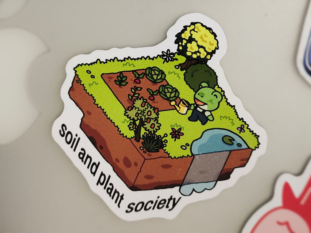 A tote bag for the Soil and Plant Society with an illustration of a frog on a floating island garden